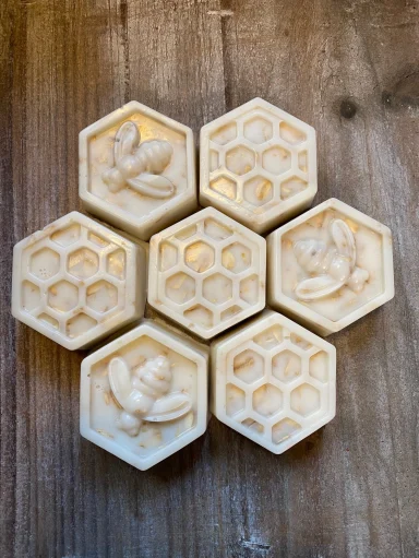 Six hexagonal wax molds with intricate designs of flowers and bees on a wooden surface.
